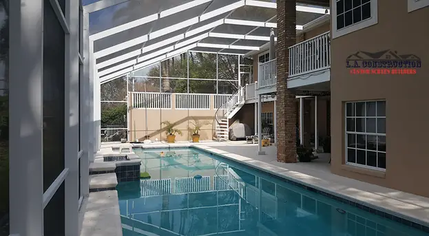 Two-story pool cage in Clermont over a long pool beside a home with an outside staircase