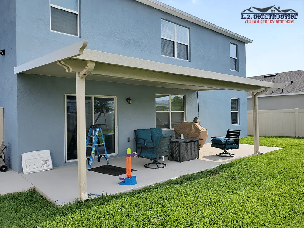 Woodgrain aluminum patio cover with decorative brackets behind a two-story home